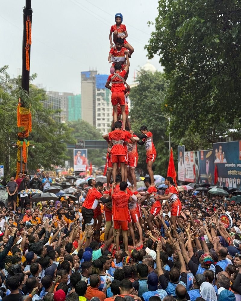A tall human pyramid of players in orange jerseys rising above a cheering street crowd – Tallest Human Pyramid world record idea